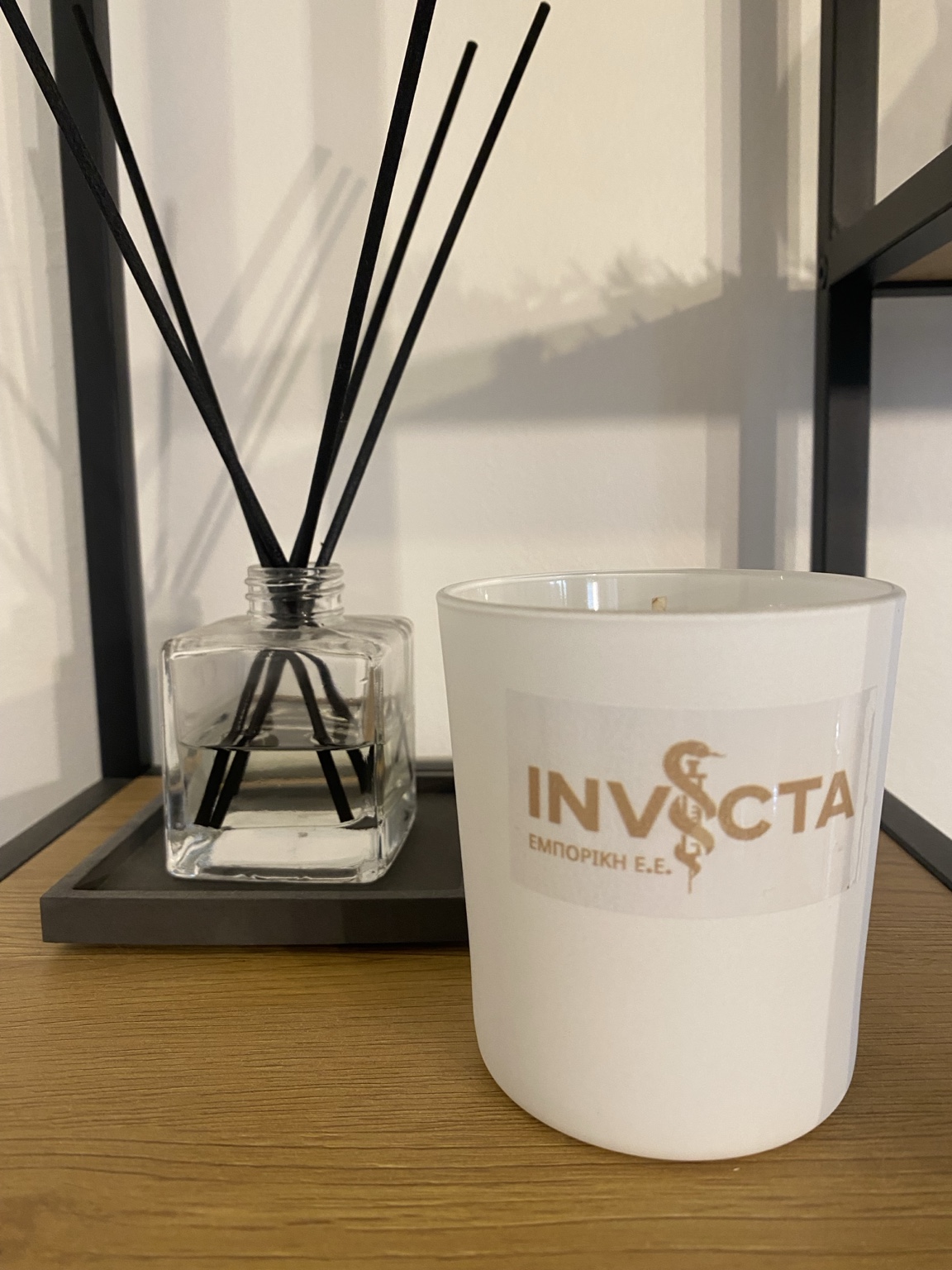 Λευκό κερί UPCALM με χρυσό λογότυπο Invicta, φωτογραφημένο σε ξύλινη επιφάνεια