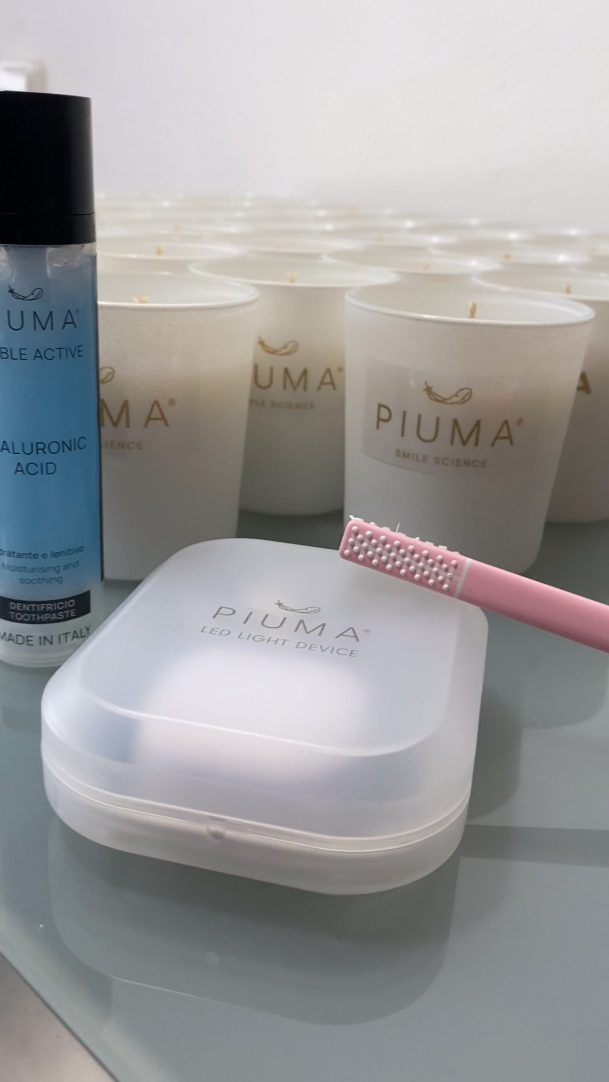 Λευκά κεριά με χρυσές ετικέτες PIUMA Smile Science δίπλα σε προϊόντα της PIUMA
